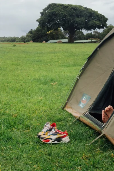 A tent on green grass with a pair of colourful sneakers outside and a bare foot poking out of the door.