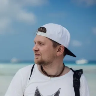 Andrii in a white cap on a beach, looking to the side.