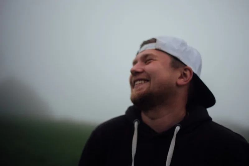 Andrii laughing in a black hoodie and white cap, in thick fog.
