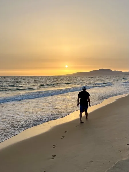 Andrii walking along a beach at sunset, leaving footprints in the wet sand.